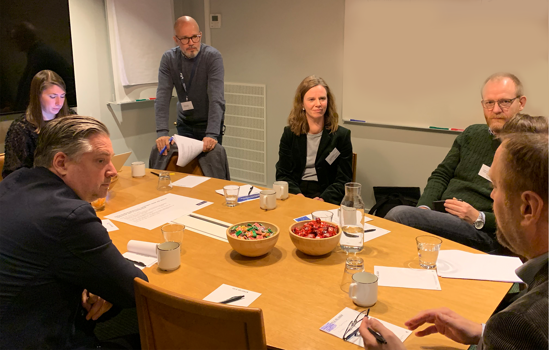 Foto på 7 personer runt ett bord som diskuterar under en workshop